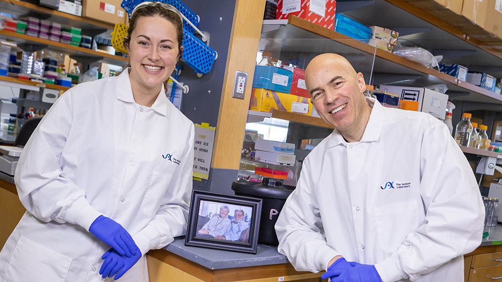 (l to r) Cara Hardy and Ron Korstanje in the Korstanje Lab with a photo of Ken and Beverly Paigen. Photo credit: Tiffany Laufer